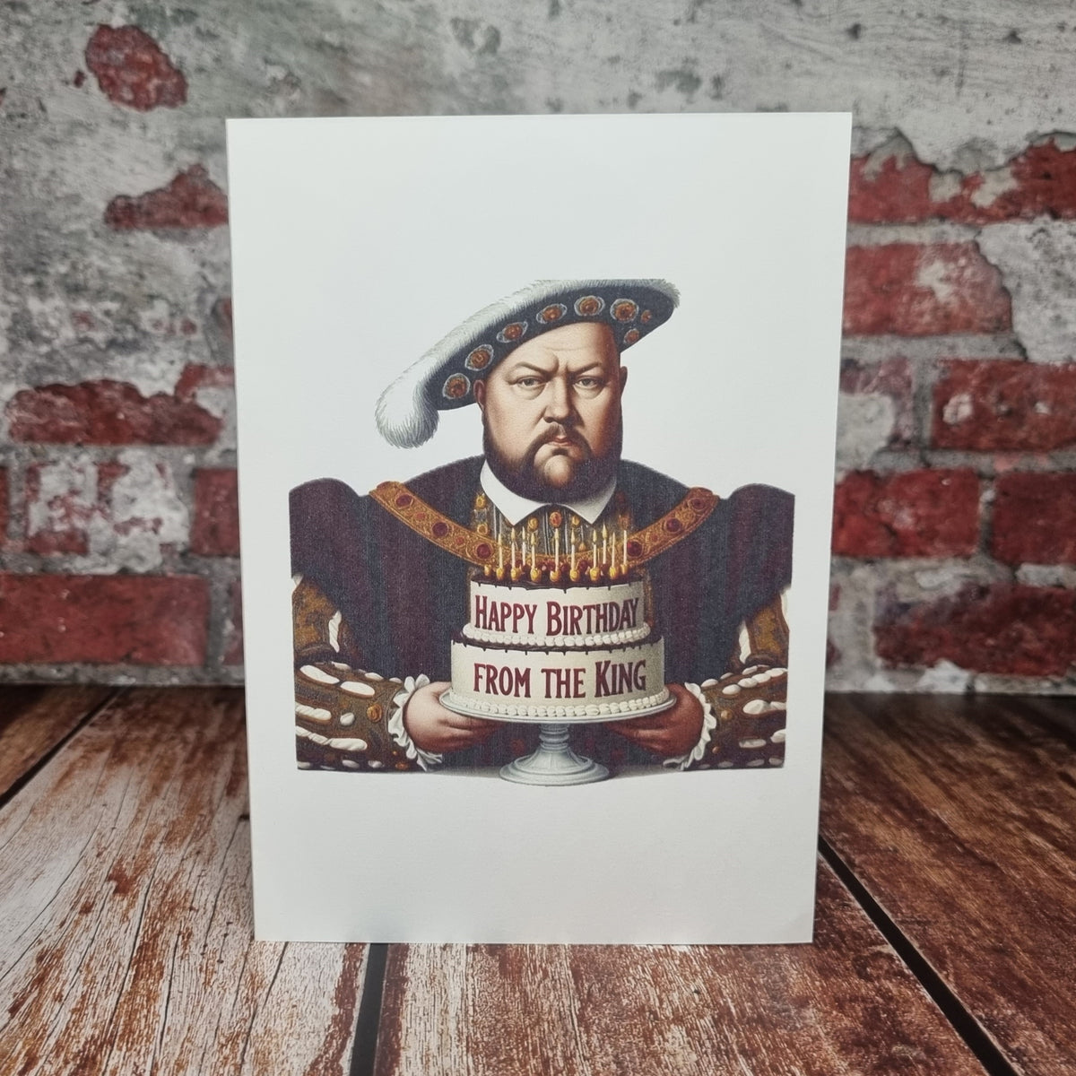 Henry VIII birthday card standing against a brick wall, the king holding a Happy Birthday banner